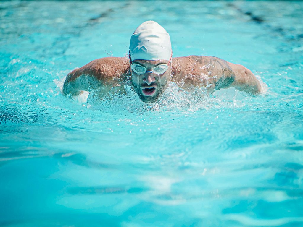 Man swimming in lanes, with white swim cap and goggles